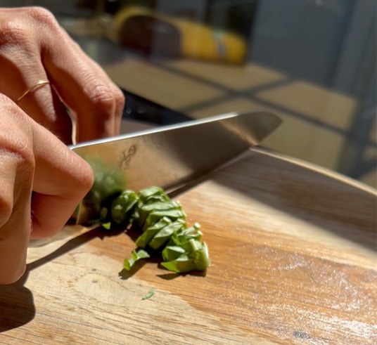Cutting basil with a knife on a cutting board.