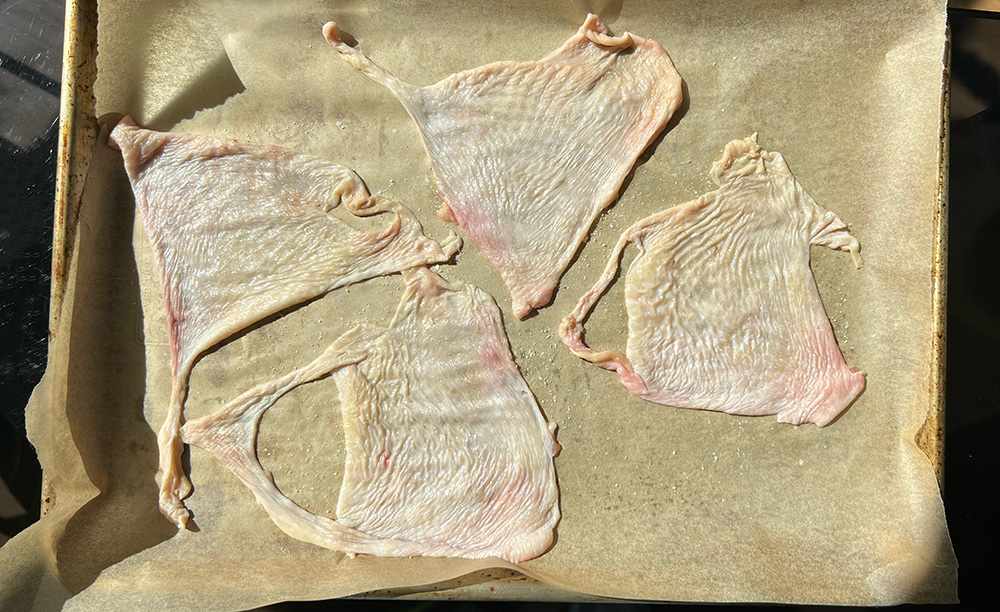Raw chicken skin on a lined baking sheet.